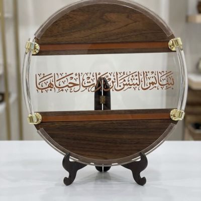 بينما يمتزج الخشب الدافئ بالشفافية الراقية، 2صينيه دائريه بتصميم يجسد الفن والجمال. لمسة فنية تزين سفرتك." ​ "A perfect harmony of warm wood and sleek clarity. This circular stand is a masterpiece of art and elegance, adding a sophisticated touc