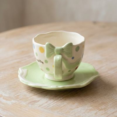 طقم فنجان وصحن سيراميك أخضر بنمط منقط وتصميم فيونكة مجسمة.&  Green Ceramic Cup and Saucer Set with Polka Dot Pattern and 3D Bow Design.
