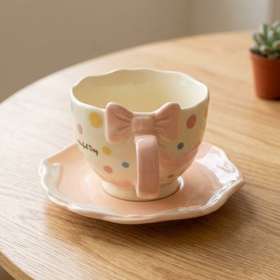 : طقم فنجان وصحن سيراميك وردي بنمط منقط وتصميم فيونكة مجسمة.% : Pink Ceramic Cup and Saucer Set with Polka Dot Pattern and 3D Bow Design.