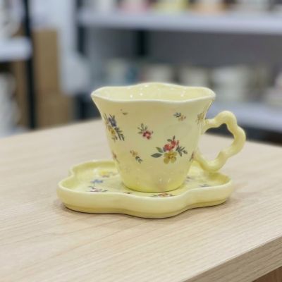  طقم فنجان وصحن سيراميك أصفر بنقوش زهور ريفية ومقبض على شكل وردة.& : Yellow Ceramic Cup and Saucer Set with Vintage Floral Patterns and Flower-Shaped Handle.