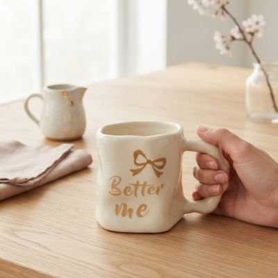 كوب سيراميك يدوي الصنع بعبارة "Better me" ونقشة فيونكة ذهبية.  &  Handmade Ceramic "Better me" Mug with Gold Bow Accent.