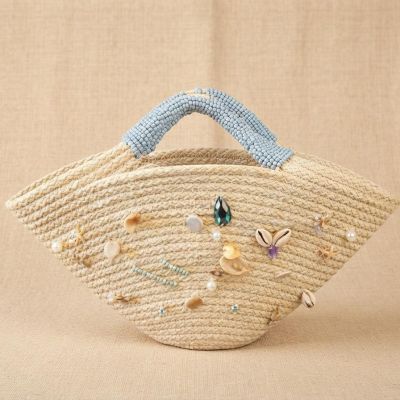 حقيبة يد قش (خوص) بتصميم هلالي مزينة بالقواقع والخرز الأزرق.  & : Flared Straw Tote Bag Decorated with Seashells and Blue Beads.