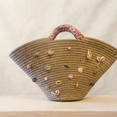 حقيبة يد قش (خوص) بتصميم هلالي مزينة بالقواقع والخرز الملون.  &  Flared Straw Tote Bag Decorated with Seashells and Colorful Beads.