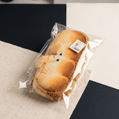 مقلمة قماشية على شكل رغيف خبز مع وجه مبتسم.Cute Bread-Shaped Plush Pencil Case with Smile Detail.