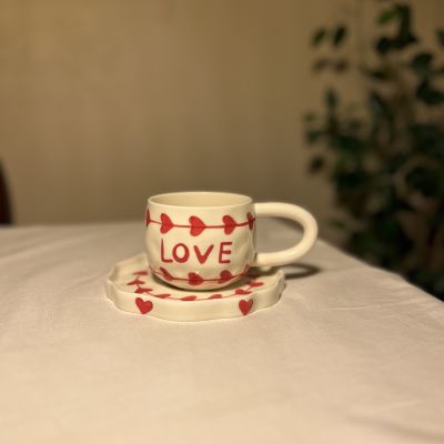 ceramic coffee cup and saucer set featuring red heart patterns and the word "LOVE"